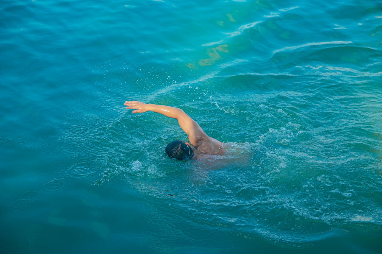 A male swimmer executes a crawl stroke in the clear turquoise waters of Vũng Tàu, Vietnam.
